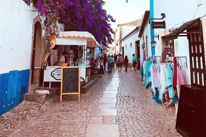 Quaint cobblestone street in Óbidos lined with shops and cafes, ideal stop on a Lisbon to Nazaré tour.