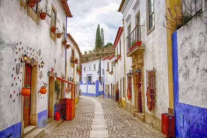 Charming cobblestone street in Óbidos, Portugal, showcasing colorful historic architecture on a private half-day tour to Óbidos and Nazaré.