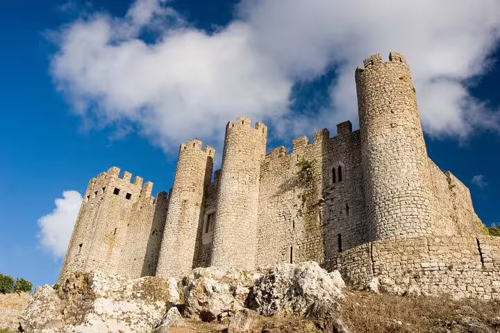 Majestic medieval castle walls under a bright blue sky, perfect for a private half-day tour of Óbidos and Nazaré.