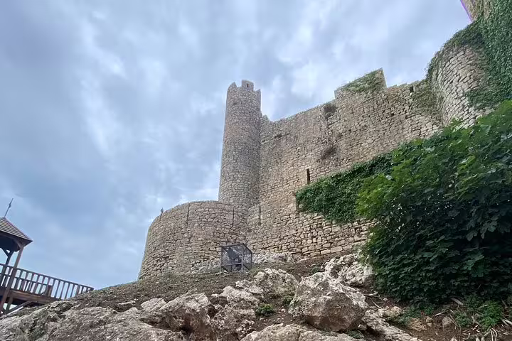 Majestic medieval castle walls in Óbidos, Portugal, showcasing ancient stonework and lush greenery under a cloudy sky.