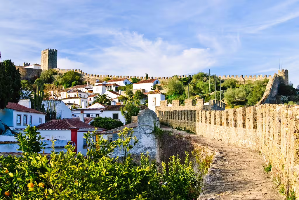 Medieval stone walls and charming white houses of Óbidos, Portugal, under a bright sky, showcasing historical and religious heritage.