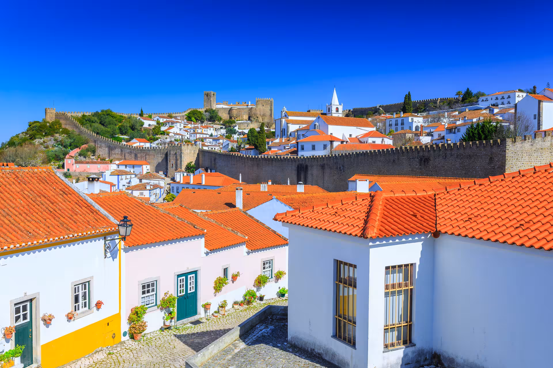 Scenic view of Óbidos with traditional white houses and red roofs, surrounded by medieval walls under a bright blue sky.
