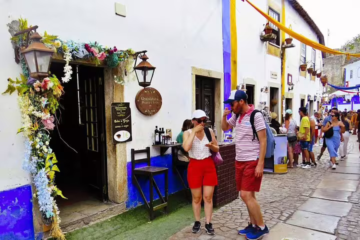 Charming street in Óbidos with tourists enjoying local shops and decorations during a lively festival day.