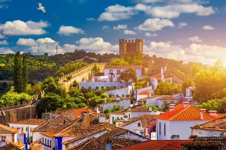 Scenic view of Óbidos village with medieval castle and vibrant rooftops, featured in a Lisbon day tour to Fátima, Nazaré, Óbidos.