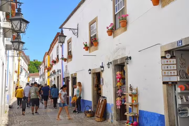 Charming street in Óbidos with whitewashed houses, colorful flower pots, and tourists exploring shops.