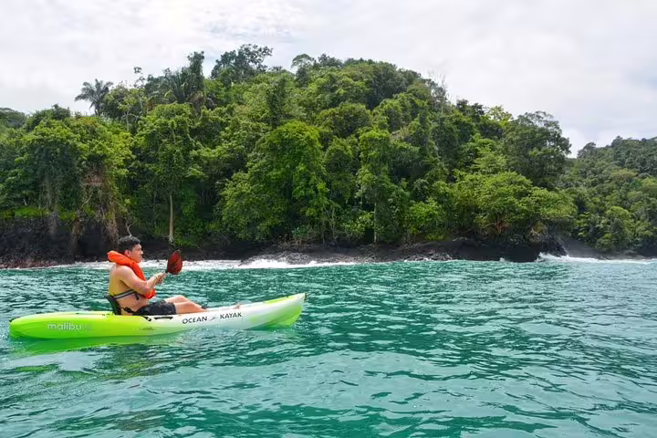 Paddler navigates the serene turquoise waters near lush jungle coastline on an Ocean Kayak in Manuel Antonio.