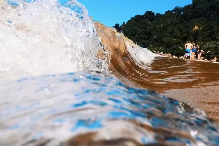 Close-up of ocean waves crashing onto a sandy beach with lush greenery, ideal for a refreshing boat tour stop.