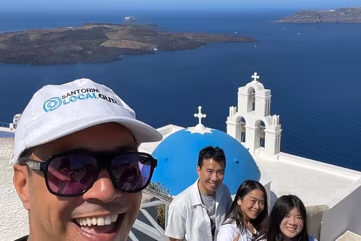 Group selfie in Oia with blue-domed church and Santorini caldera views on 8-hour Thera island tour