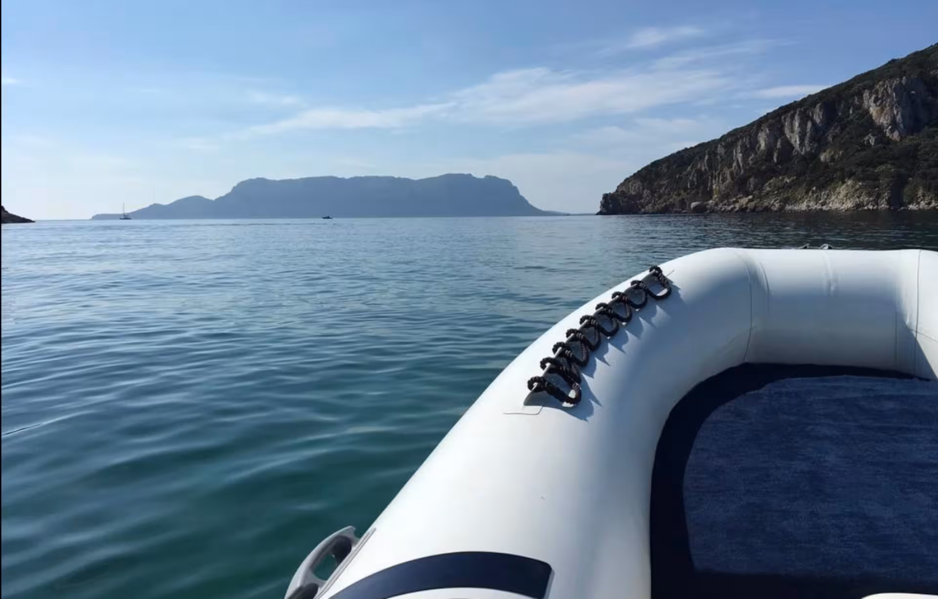 Boat approaching Tavolara Island's picturesque coastline, highlighting a serene and clear sea view from Porto San Paolo.