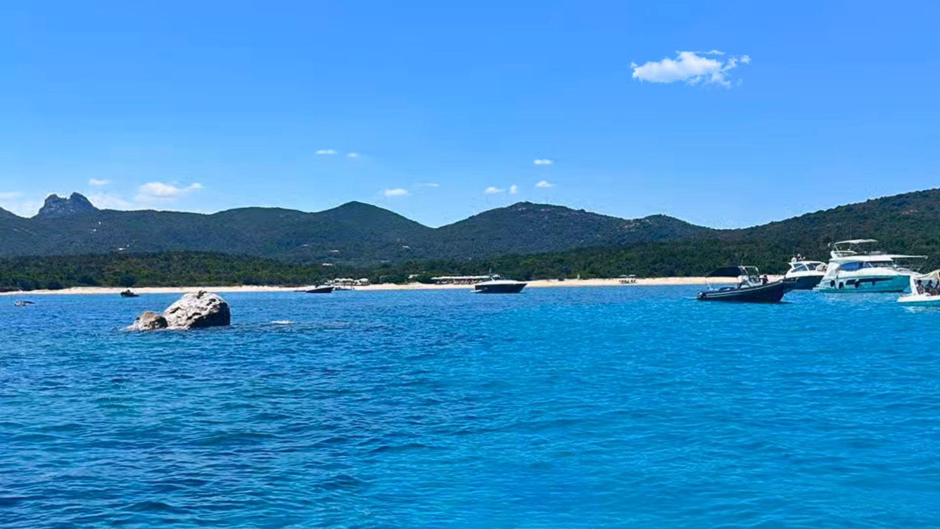 Scenic view of Capo Figari's turquoise waters with boats and lush hills on an Olbia dolphin-watching tour.