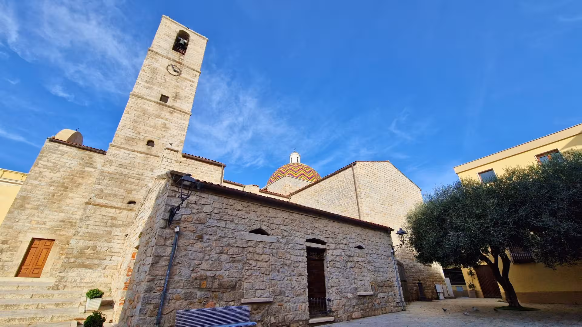 Historic stone church with colorful dome under a clear blue sky in Olbia, ideal for cultural tours in Sardinia.