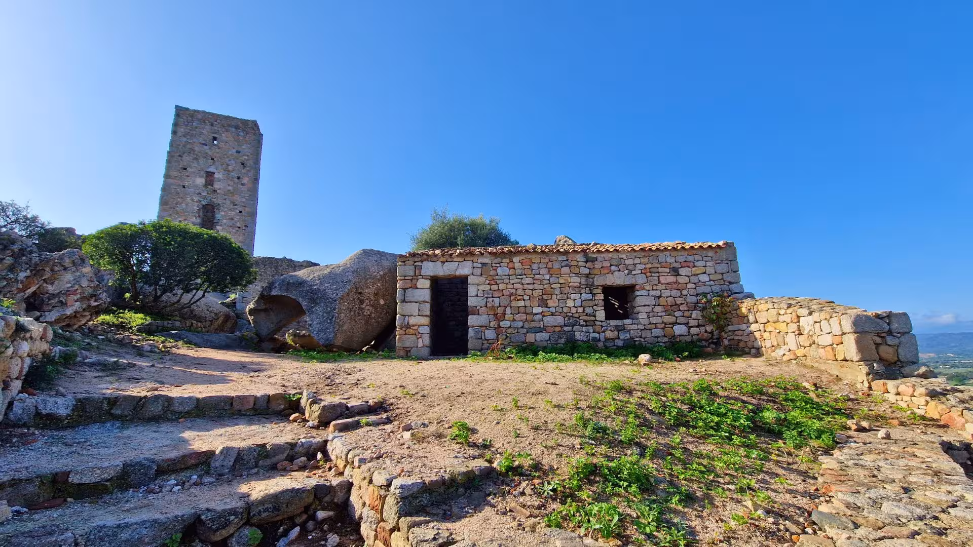 Medieval stone tower and rustic building on a hill in Olbia, ideal for historical tours in Sardinia's scenic landscapes.