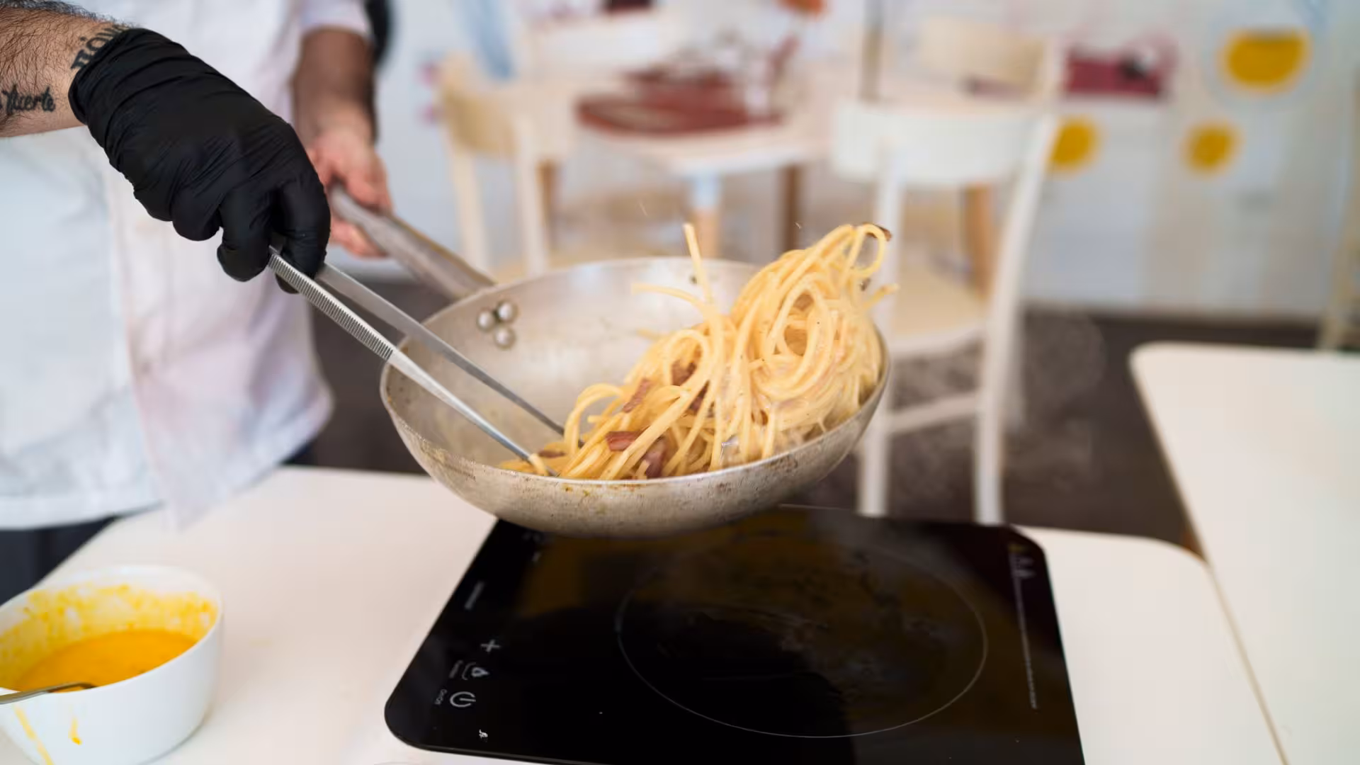 Chef tossing spaghetti in a pan during Olbia's authentic pasta carbonara cooking class experience.