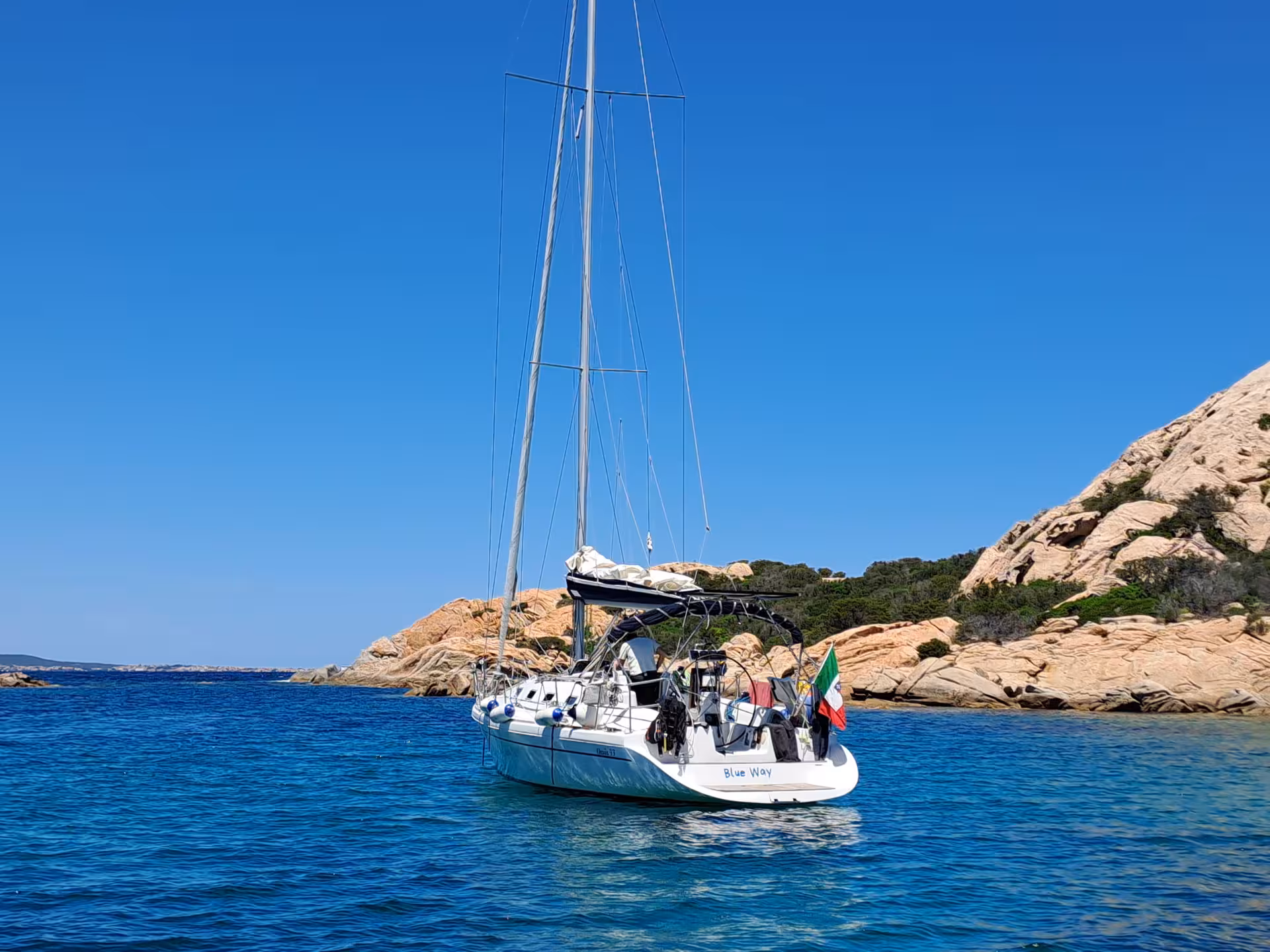Sailboat anchored near rocky shores with crystal-clear waters on the Tavolara and Cala Moresca sailing tour from Olbia.