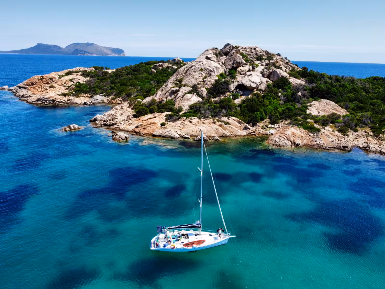 A sailboat drifts in the turquoise waters near rocky shores on the Olbia sailing tour to Tavolara and Cala Moresca.