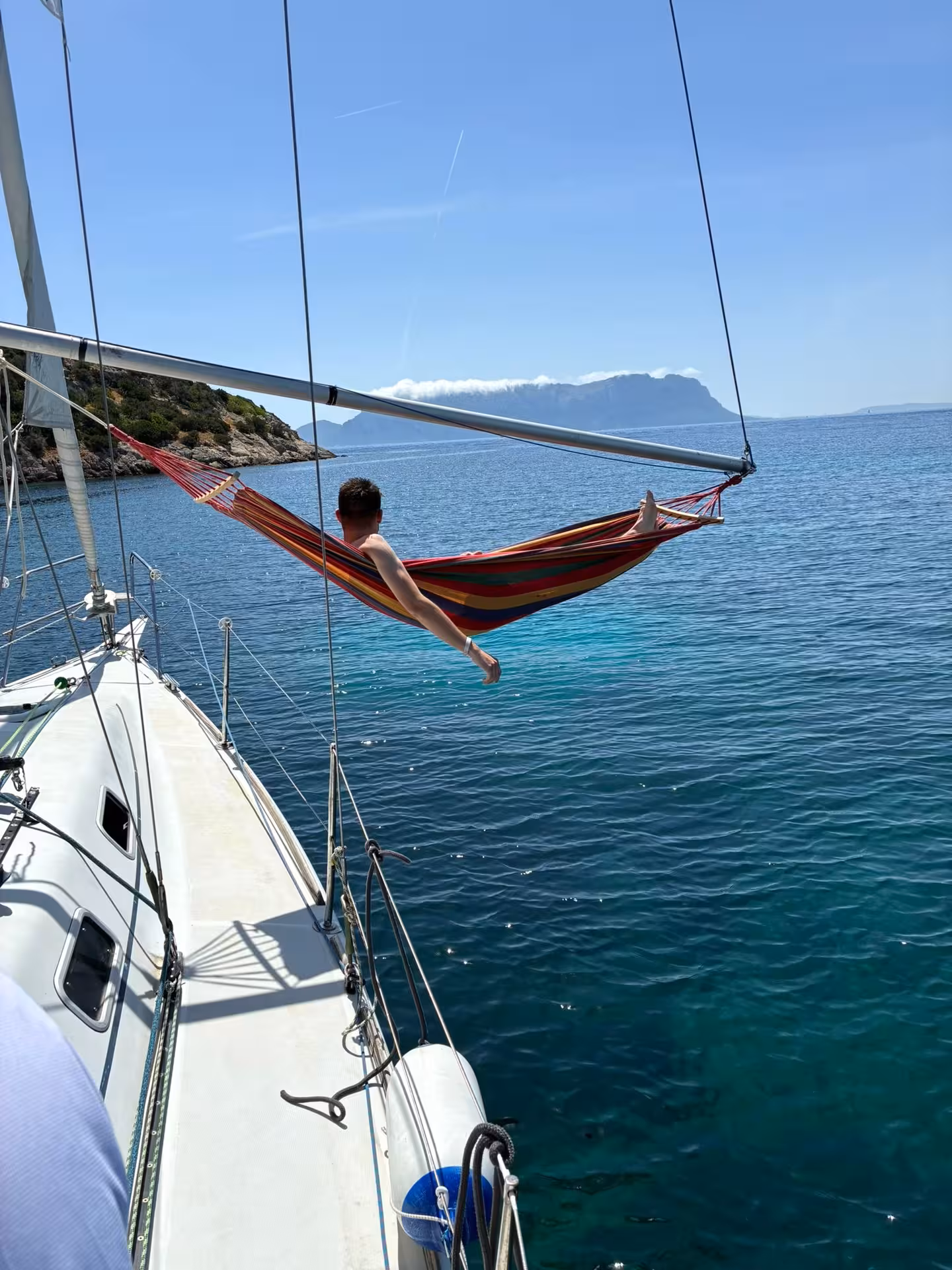 Relaxing on a hammock aboard a sailboat with views of Tavolara's stunning coastline and crystal-clear waters.