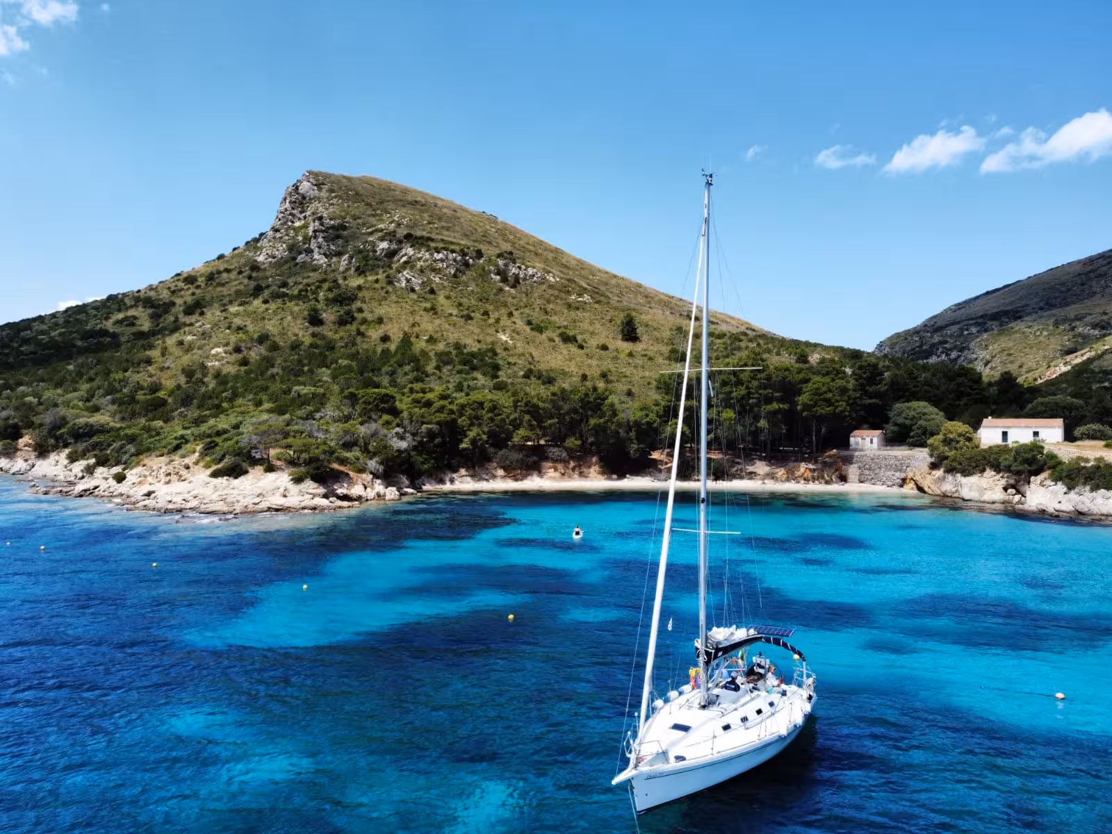 A sailboat glides through the crystal-clear turquoise waters near Tavolara Island, surrounded by lush green hills.