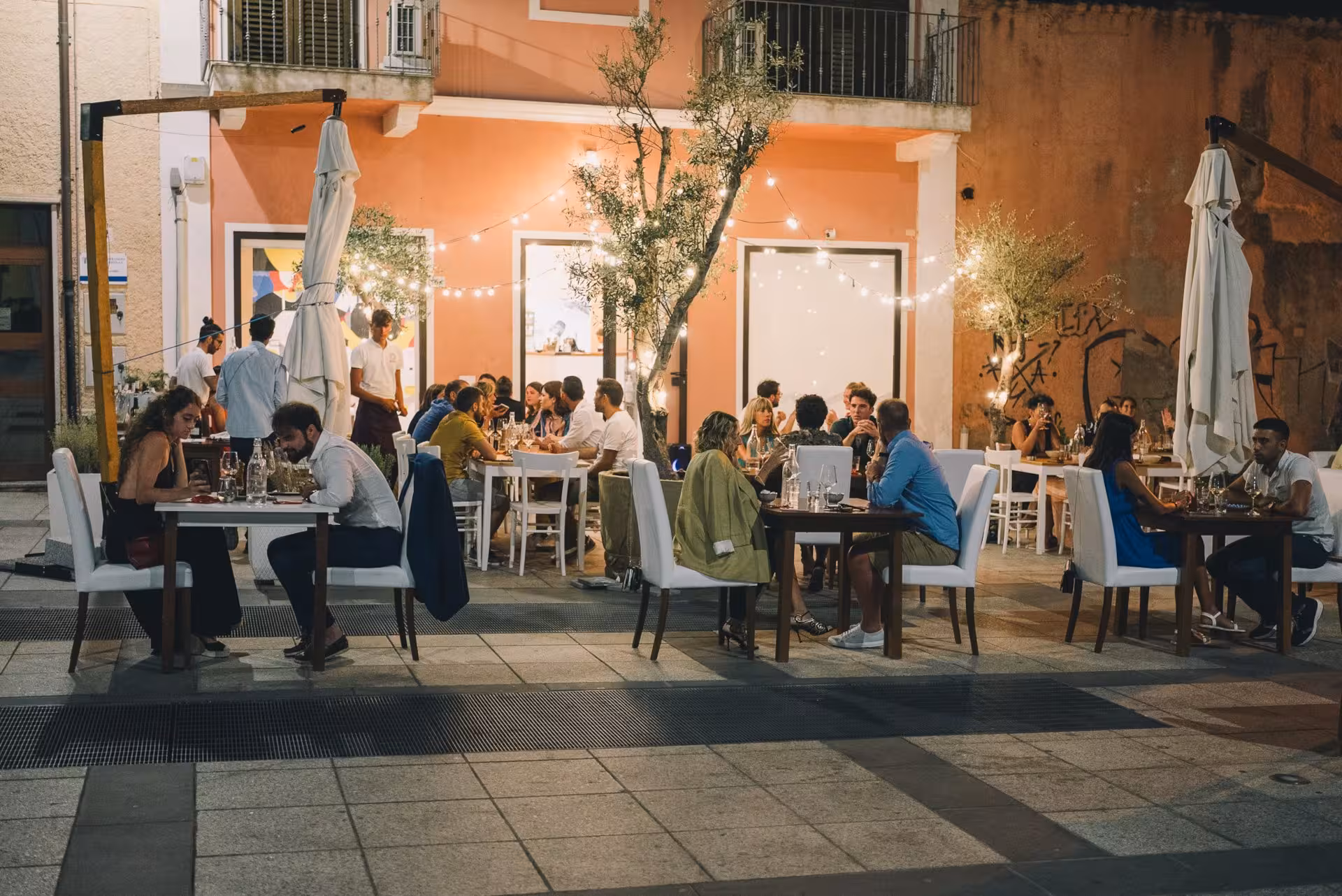 Outdoor dining scene in Olbia with people enjoying Sardinian tapas under string lights at a cozy restaurant.