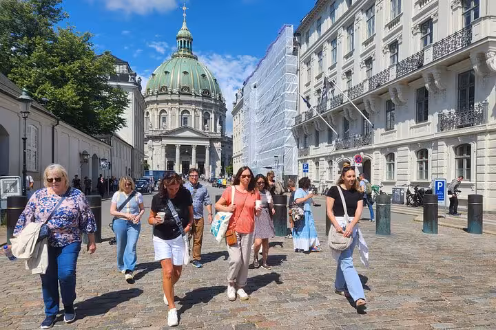 Group of tourists explores Old Copenhagen, walking towards a historic dome under a bright blue sky.
