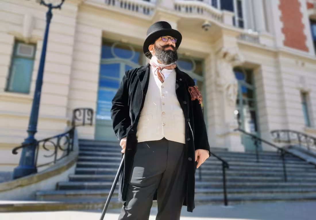 Bearded guide in Victorian top hat and black coat with cane outside historic Lille building