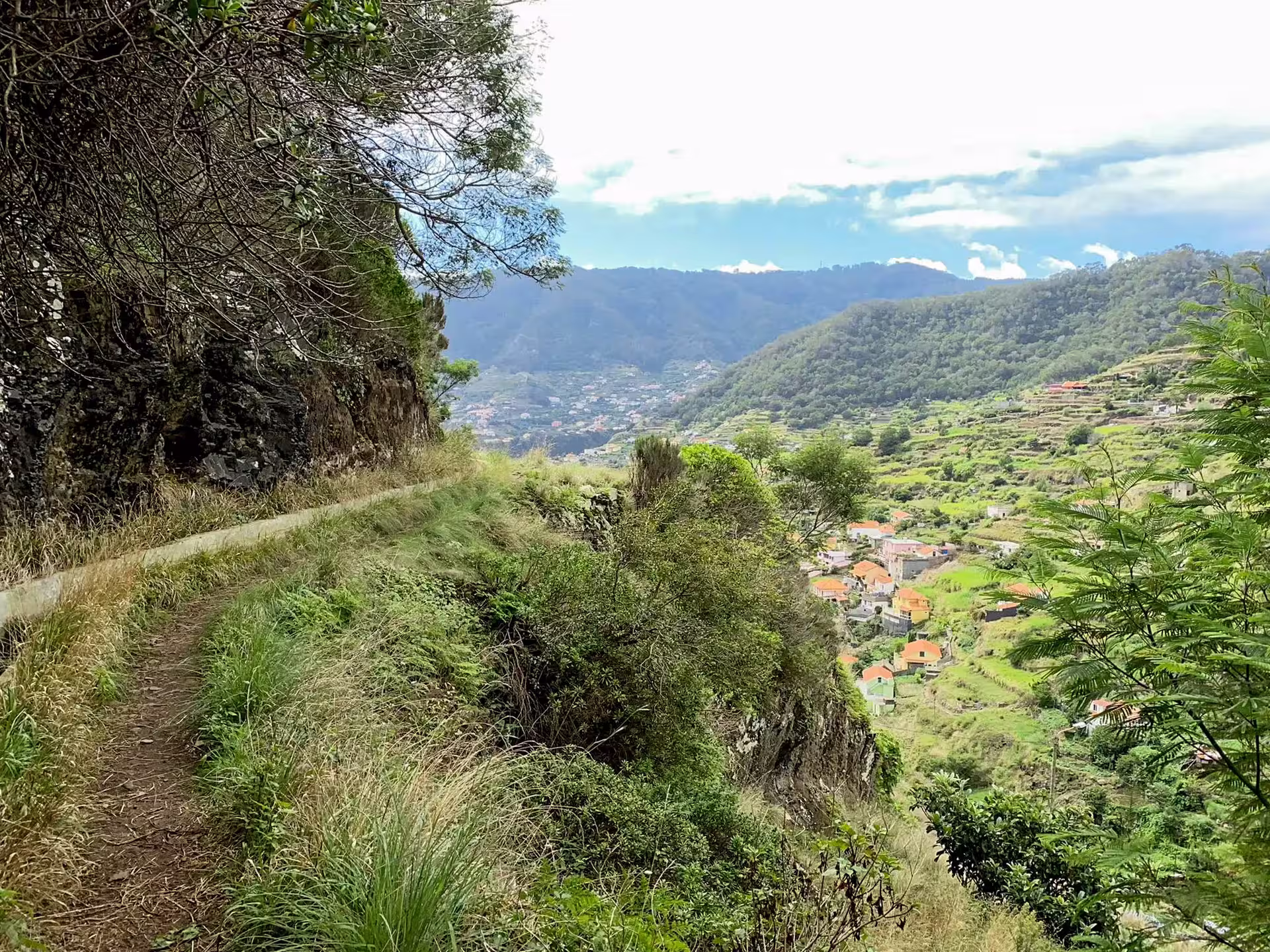Scenic hiking trail on The Old Path, lined with greenery and overlooking a picturesque valley and distant mountains.