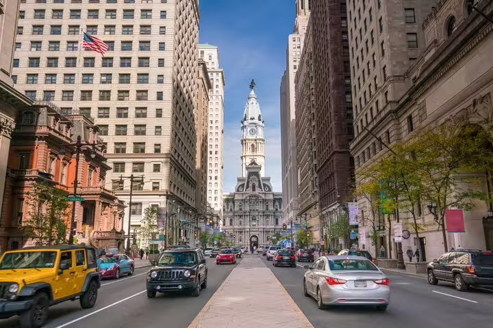 Busy street view of Philadelphia City Hall tower along a traffic-filled urban boulevard with historic buildings