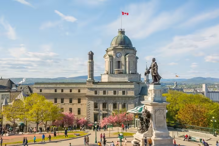 Historic Old Quebec City skyline with domed building, Samuel de Champlain statue, and Canadian flag on sunny day