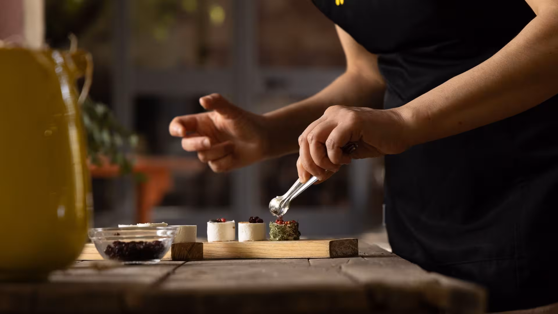 Artisan arranges gourmet goat cheese with herbs and berries for tasting in Oliena, showcasing Sardinian culinary traditions.