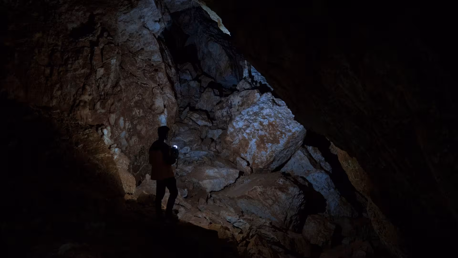 Explorer with headlamp illuminating rocky interior of Sa Nurre de Su Hoda cave in Oliena trek.