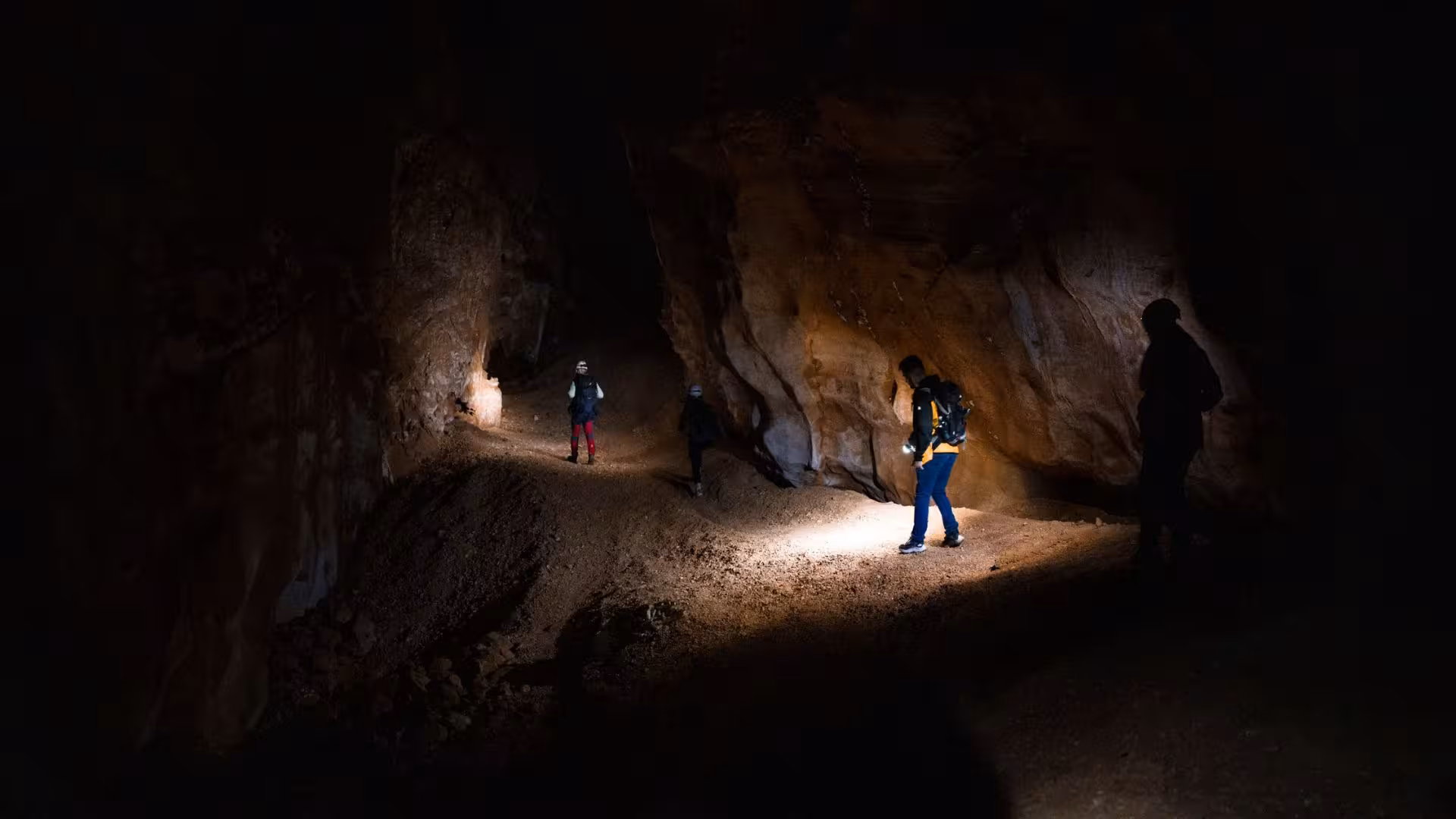 Trekkers navigating the rugged path inside Sa Nurre de Su Hoda cave, Oliena, illuminated by flashlights.