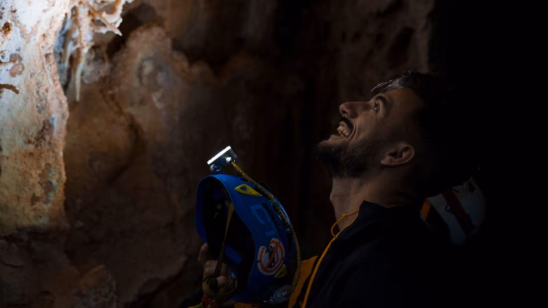 Adventurer gazing at cave formations with a helmet in hand during Oliena trekking expedition.