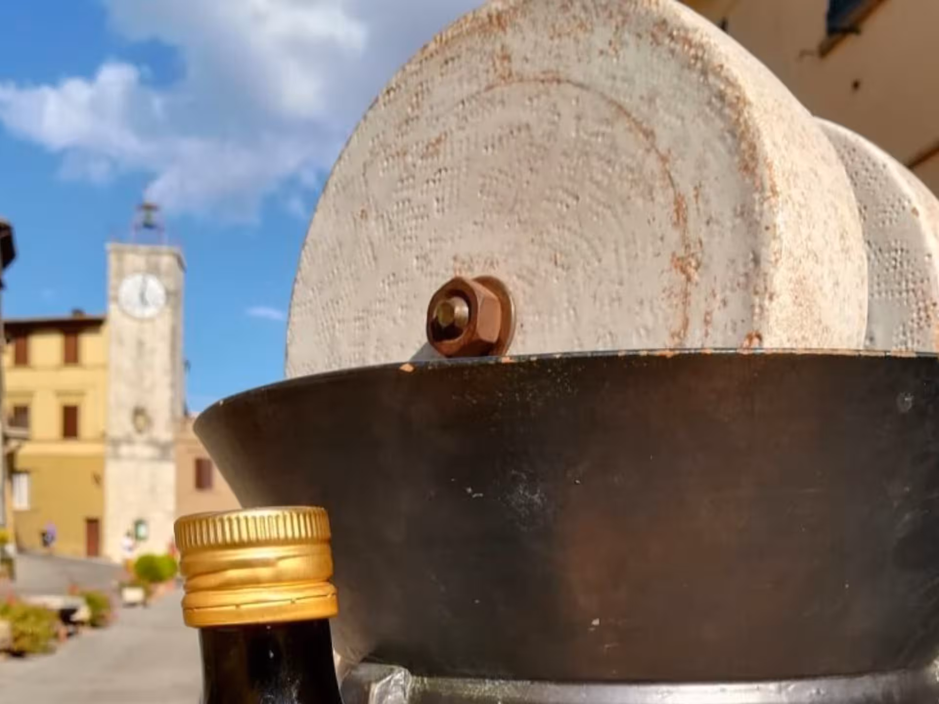 Traditional olive oil mill with stone press and bottle in scenic Chianciano town square.