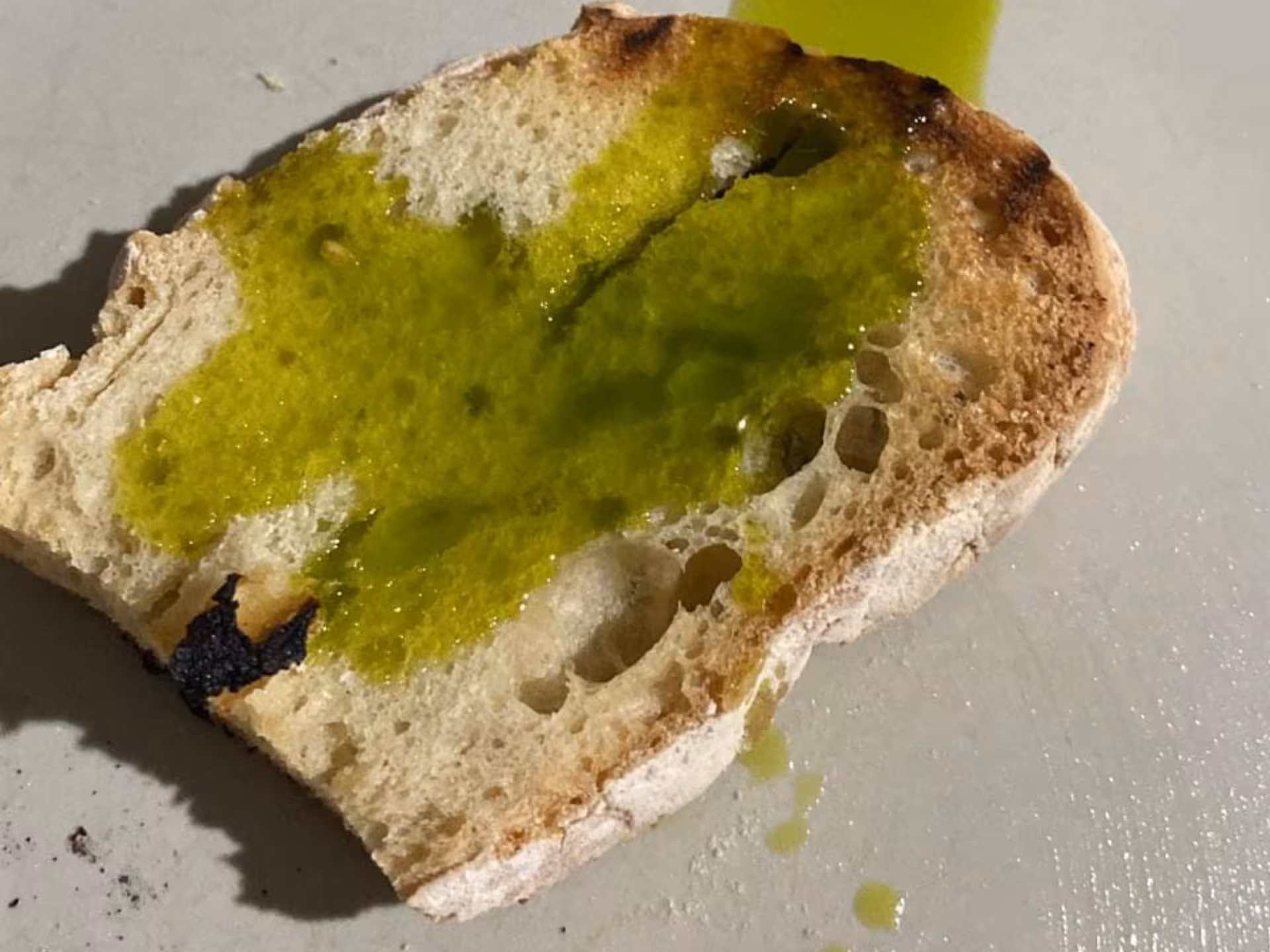 Slice of rustic bread drizzled with vibrant green olive oil during a tasting in Perugia.