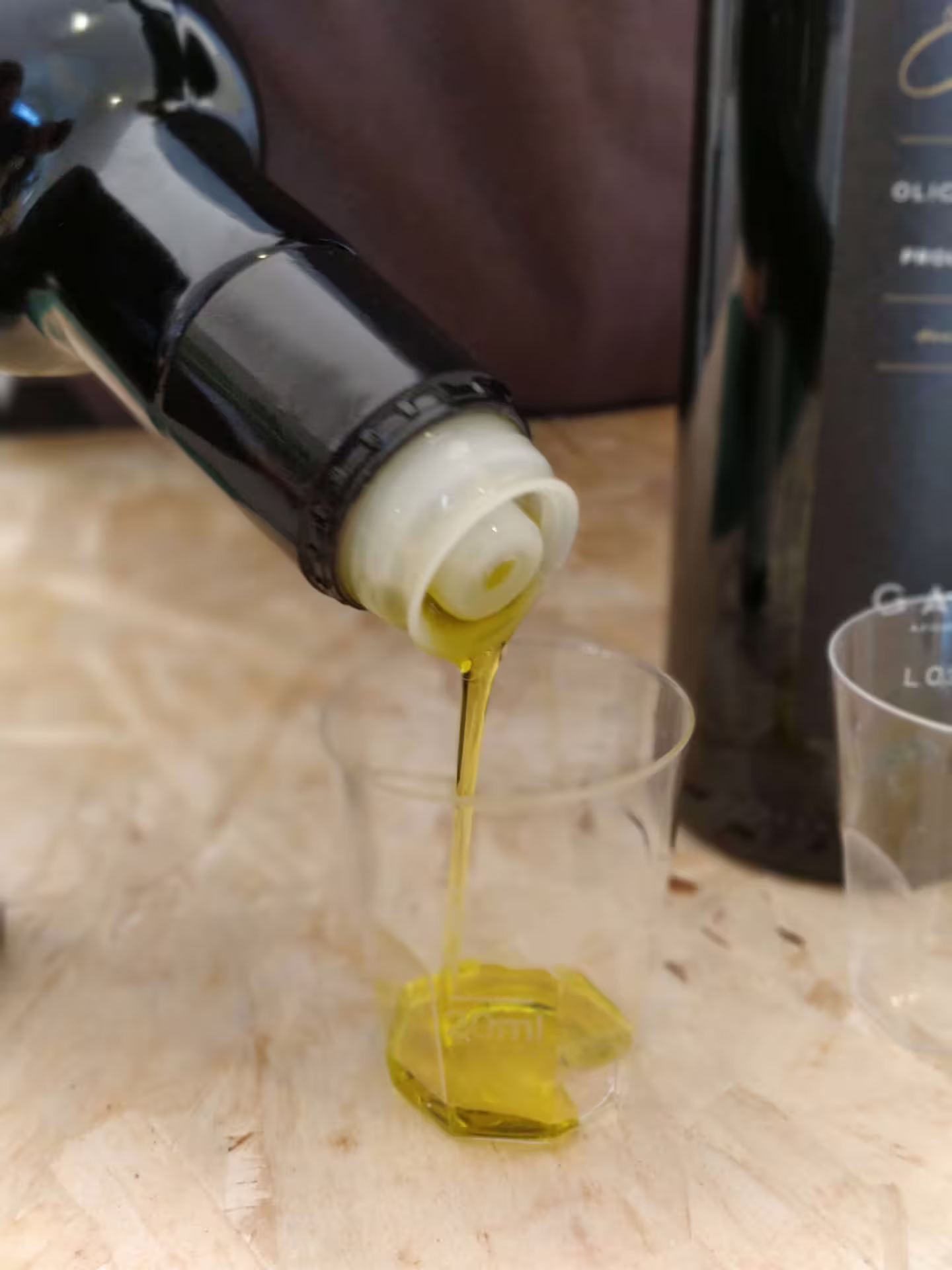 Degustazione di olio extravergine: versamento in bicchierino durante esperienza raccolta olive in frantoio