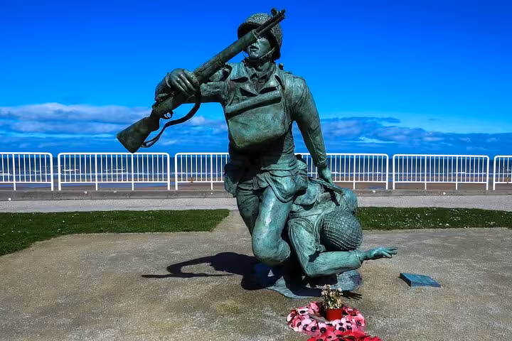 Bronze WWII soldier statue carrying fallen comrade at Omaha Beach D-Day memorial, Normandy