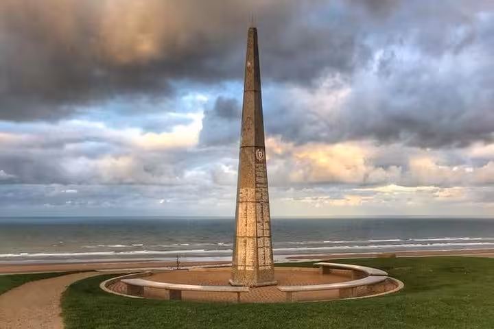 Obelisk memorial monument overlooking Omaha Beach on the Normandy coast under dramatic cloudy skies