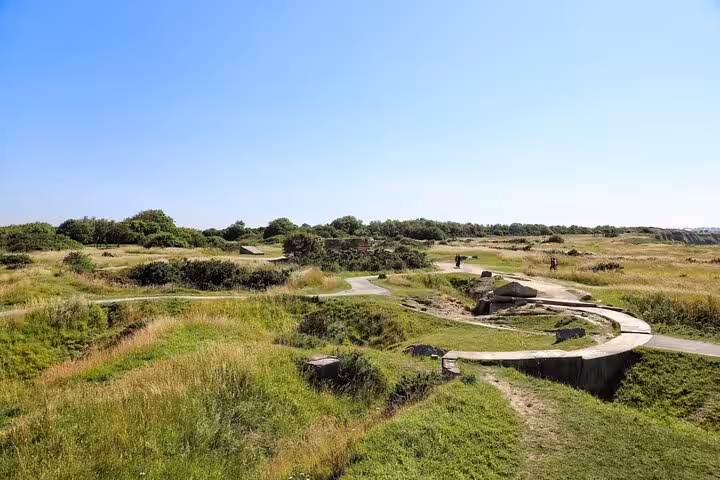 WWII gun battery ruins with curved concrete emplacements and grassy dunes at Normandy D-Day site