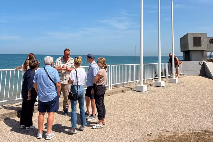 Tour group listening to guide at Omaha Beach memorial overlook with English Channel in background