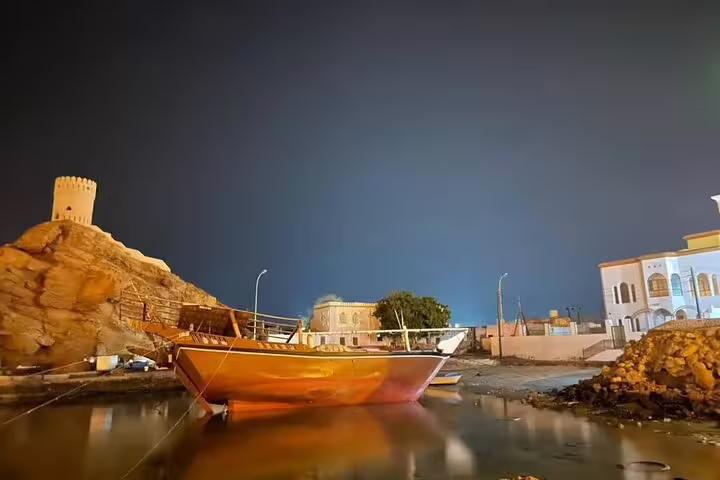 Traditional Omani boat docked at night with a historic fort in the background, featured in a 3-day Oman private tour.