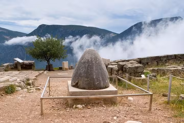 Omphalos stone at Delphi archaeological site with mountain clouds, on a 2-day luxury private tour from Athens
