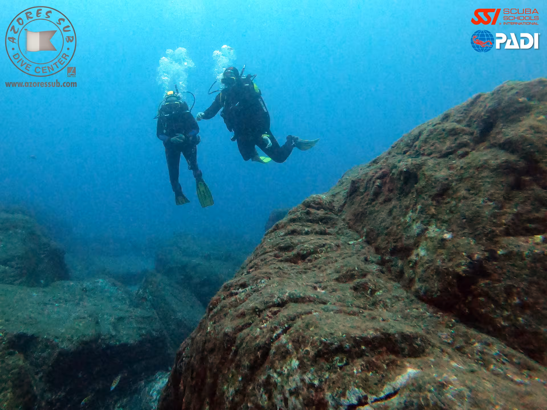 Open Water Diver training dive with two scuba divers hovering by volcanic rock reef in clear Azores waters