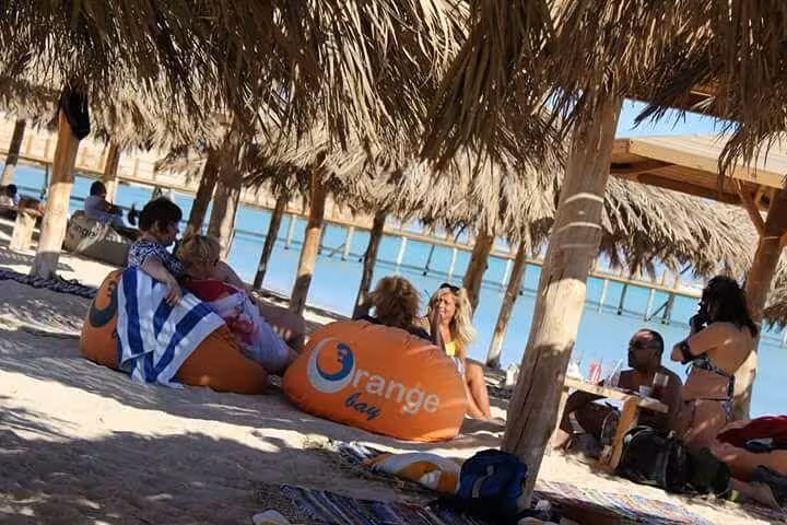 Guests relaxing on Orange Bay Hurghada beach under palm huts with bean bags and Red Sea views