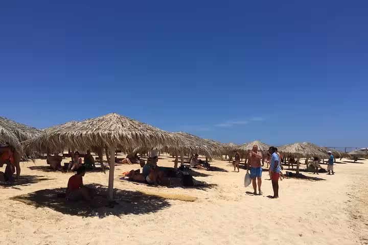 Orange Bay island beach area with straw umbrellas and loungers, ideal stop on Hurghada full-day snorkeling tour