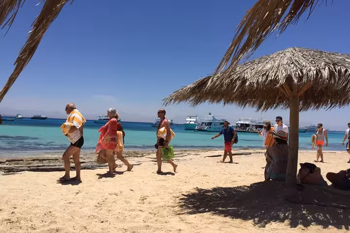 Tourists walking on Orange Bay shore with straw parasols and yachts, Red Sea island stop from Hurghada