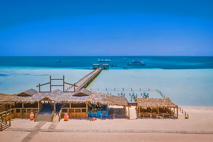 Orange Bay jetty and beach huts with boats offshore, full-day snorkeling tour from Hurghada to Giftun