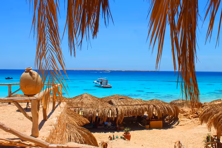 Orange Bay Island day trip beach huts and palm shade with boat on turquoise Red Sea near Hurghada