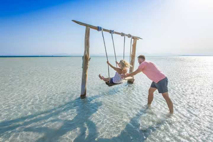 Couple enjoying the famous Orange Bay Island swing in crystal-clear Red Sea water on snorkeling day trip