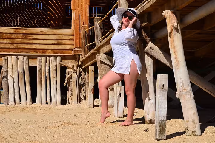Traveler posing on Orange Bay beach by rustic wooden cabanas, part of snorkeling and water sports day trip