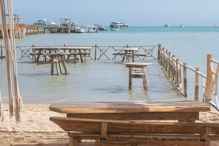 Orange Bay beach picnic tables by the shallow lagoon with boats offshore, ideal Red Sea snorkeling day trip