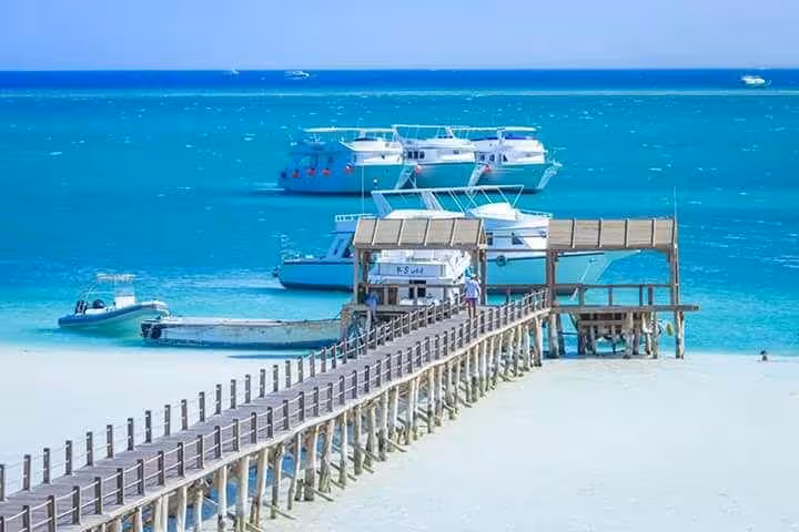 Orange Island boat trip from Hurghada with pier over white sand, yachts offshore, and crystal Red Sea water